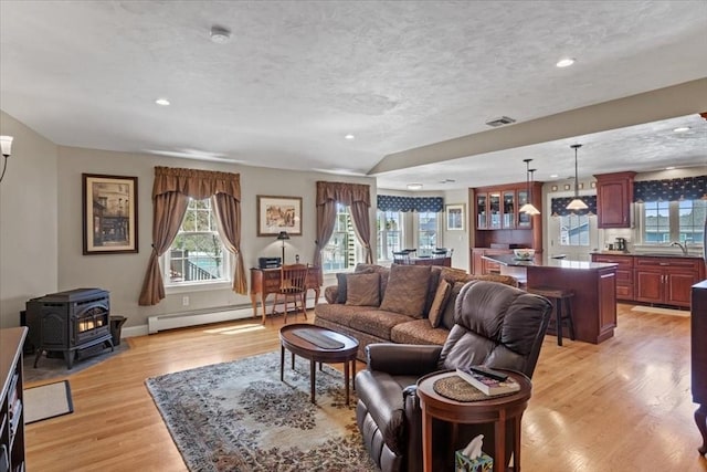 living room featuring light wood-type flooring, a wood stove, plenty of natural light, and a baseboard heating unit