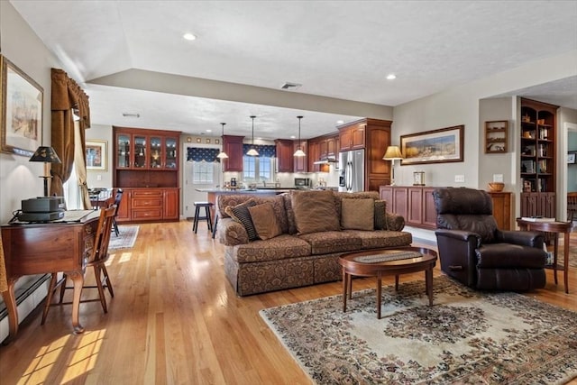 living area featuring visible vents, a baseboard radiator, light wood finished floors, and recessed lighting