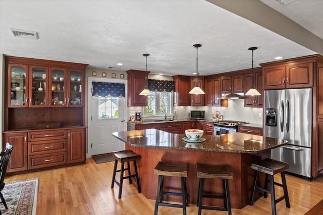 kitchen with appliances with stainless steel finishes, a breakfast bar, a sink, a center island, and under cabinet range hood