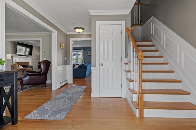 staircase with a brick fireplace, wood finished floors, a wainscoted wall, a baseboard radiator, and a decorative wall