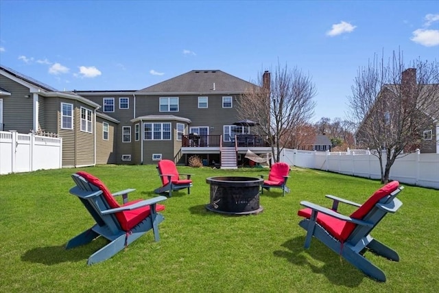 rear view of property with a fenced backyard, a fire pit, a wooden deck, and a yard