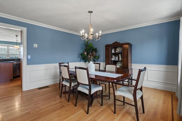 dining space featuring visible vents, wainscoting, a chandelier, light wood-style floors, and ornamental molding