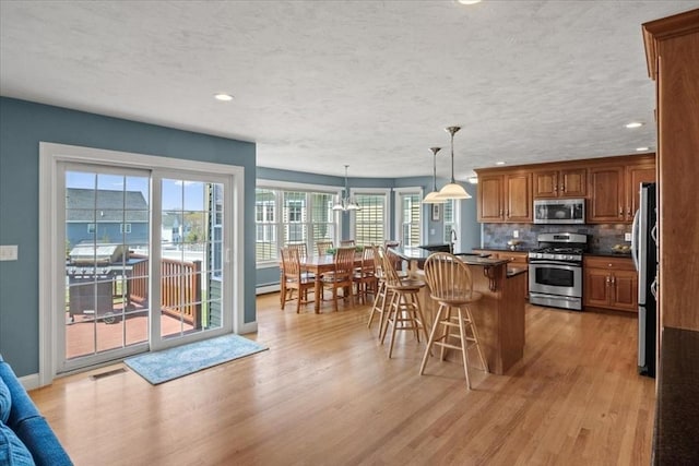 kitchen featuring a kitchen breakfast bar, brown cabinetry, stainless steel appliances, and light wood finished floors