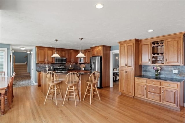 kitchen featuring a breakfast bar area, stainless steel appliances, light wood finished floors, and tasteful backsplash