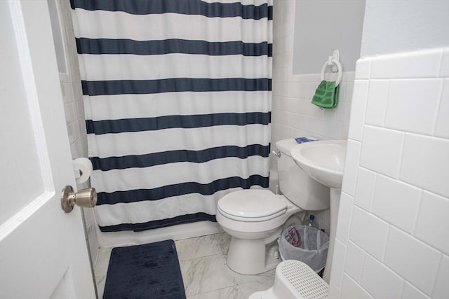 full bathroom featuring curtained shower, toilet, tile walls, marble finish floor, and wainscoting