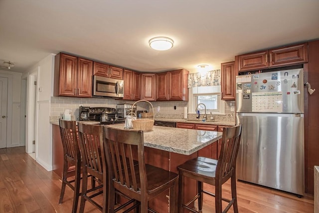 kitchen with a kitchen breakfast bar, appliances with stainless steel finishes, backsplash, and light wood-style floors