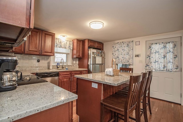 kitchen featuring light wood-style flooring, a sink, appliances with stainless steel finishes, backsplash, and a kitchen bar