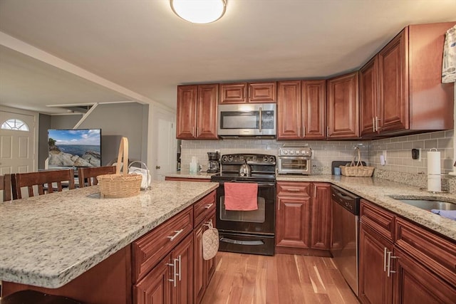 kitchen featuring light wood-style flooring, appliances with stainless steel finishes, backsplash, and light stone counters