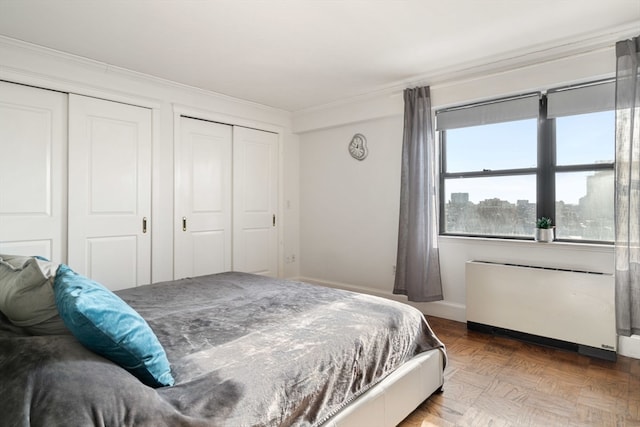 bedroom with radiator, crown molding, multiple closets, and parquet floors