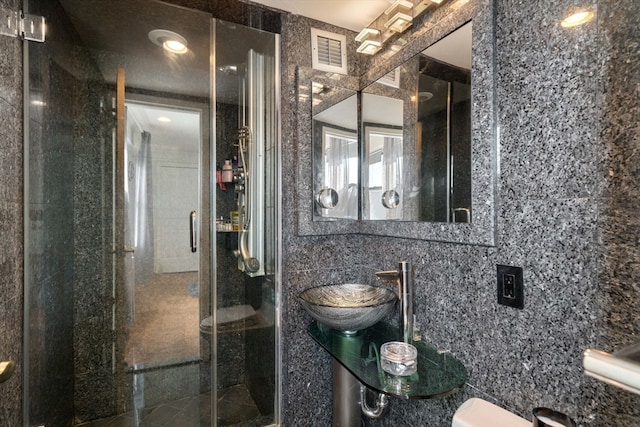 bathroom featuring toilet, a shower with shower door, sink, and tile walls