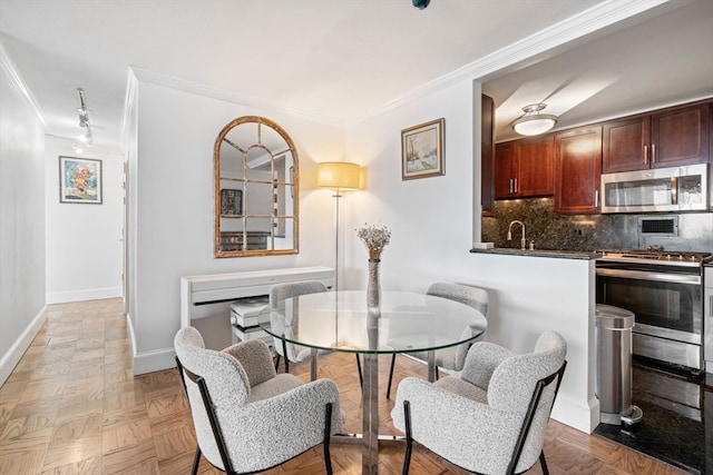 dining area featuring sink, crown molding, track lighting, and light parquet flooring