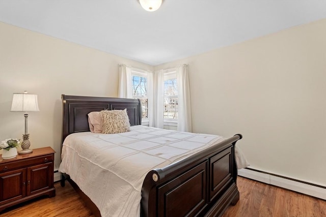 bedroom with a baseboard heating unit and light wood-style flooring