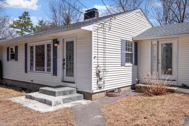 entrance to property featuring a shingled roof and a chimney