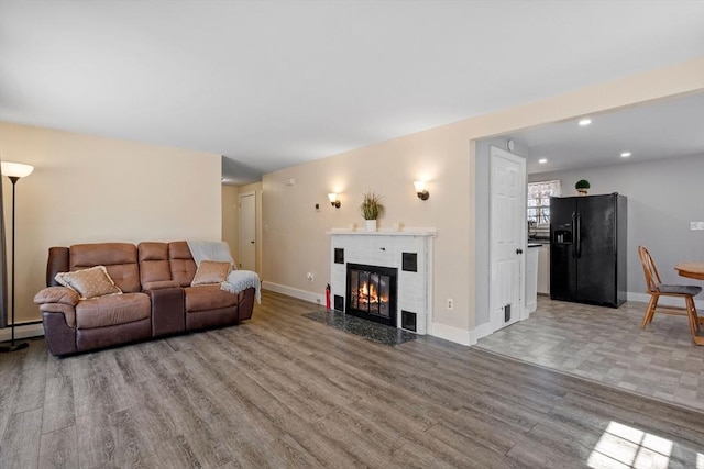 living area featuring recessed lighting, wood finished floors, a baseboard heating unit, baseboards, and a fireplace