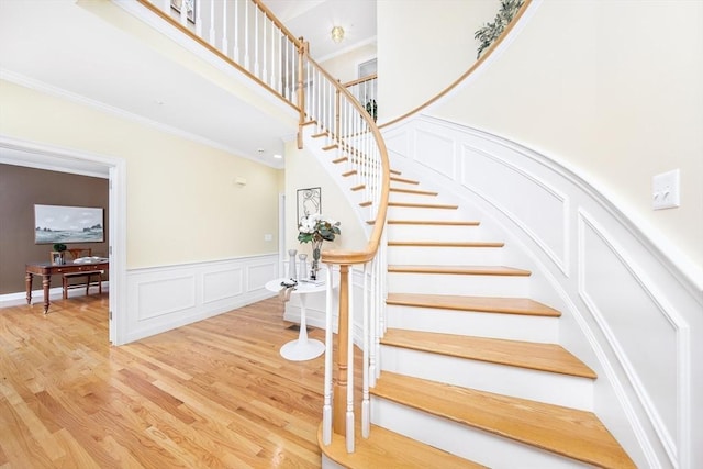 stairs featuring a decorative wall, wood finished floors, a high ceiling, and ornamental molding