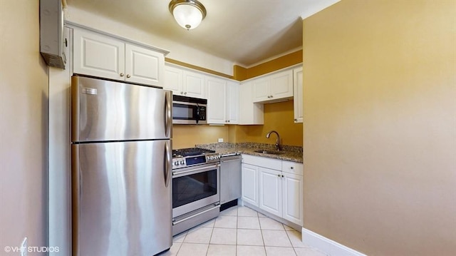 kitchen with sink, light tile patterned floors, appliances with stainless steel finishes, white cabinetry, and dark stone counters