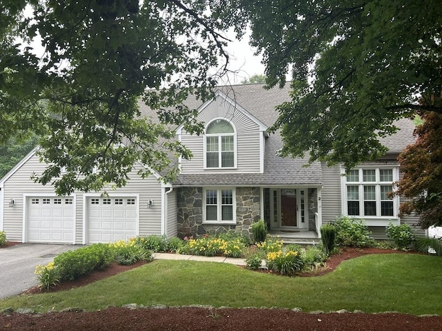 view of front of home featuring a shingled roof, aphalt driveway, a front yard, a garage, and stone siding