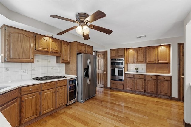 kitchen featuring light wood finished floors, beverage cooler, light countertops, brown cabinets, and appliances with stainless steel finishes