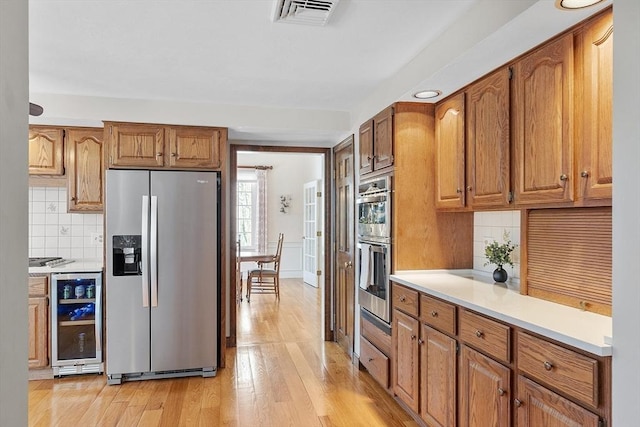 kitchen with light wood-type flooring, visible vents, wine cooler, appliances with stainless steel finishes, and light countertops