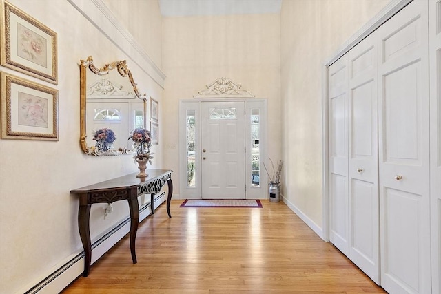 foyer entrance with baseboards, light wood-style flooring, and a towering ceiling