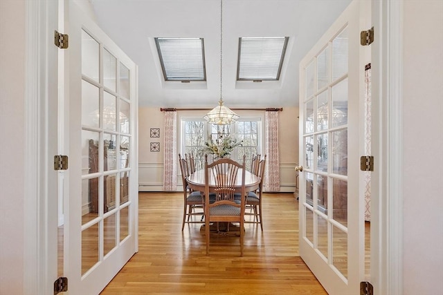 dining area with french doors, light wood-style floors, an inviting chandelier, and a baseboard radiator