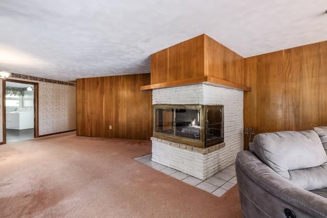 unfurnished living room with light carpet, wood walls, washer / clothes dryer, and a stone fireplace