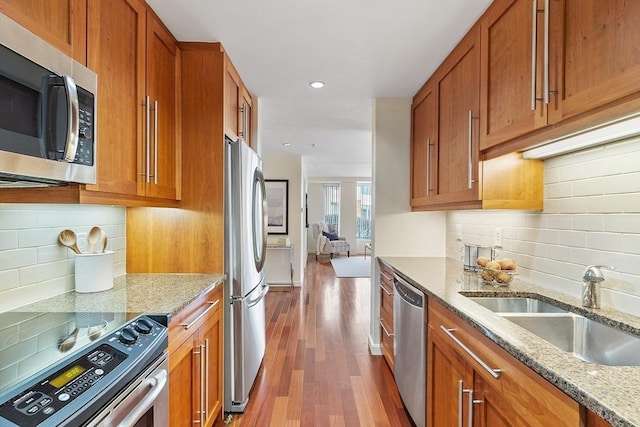 kitchen with wood finished floors, light stone countertops, a sink, stainless steel appliances, and brown cabinets