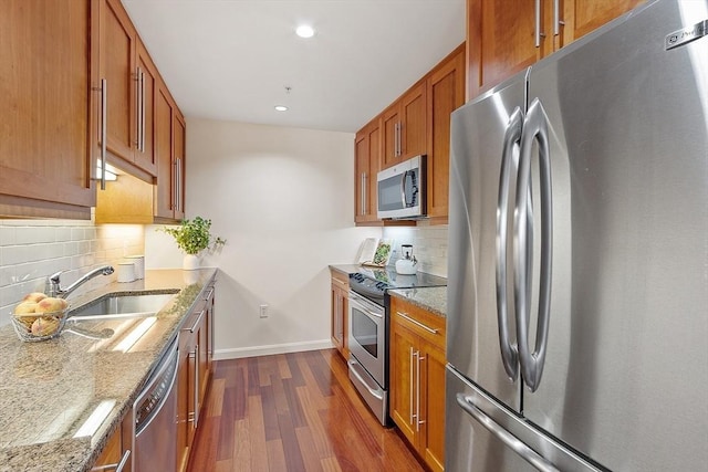 kitchen featuring baseboards, dark wood finished floors, light stone counters, brown cabinetry, and stainless steel appliances