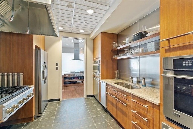 kitchen with a sink, island range hood, brown cabinetry, stainless steel appliances, and dark tile patterned flooring