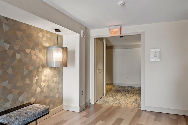 hall featuring wallpapered walls, light wood-type flooring, and baseboards