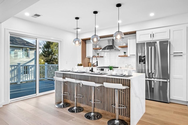kitchen with stainless steel fridge with ice dispenser, wall chimney exhaust hood, tasteful backsplash, light wood finished floors, and recessed lighting