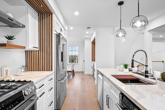 kitchen with a sink, stainless steel appliances, white cabinetry, wall chimney exhaust hood, and light stone counters