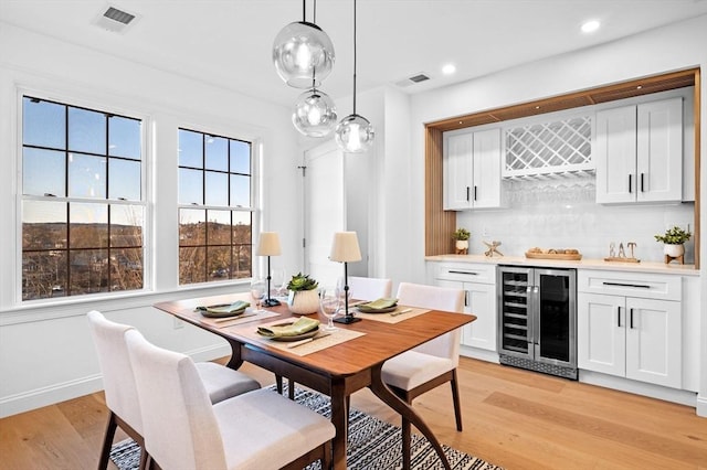 dining space with beverage cooler, a dry bar, light wood-type flooring, recessed lighting, and baseboards