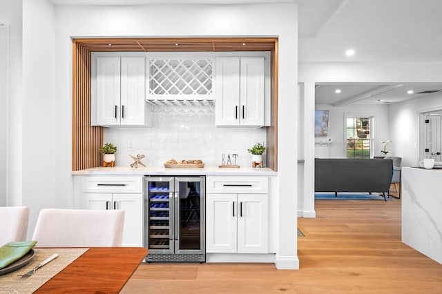 indoor dry bar with beverage cooler, decorative backsplash, light wood-style flooring, and recessed lighting