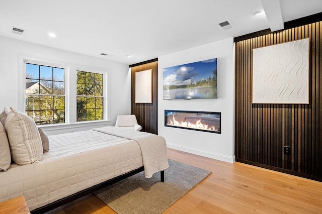 bedroom featuring wood finished floors, a glass covered fireplace, and recessed lighting