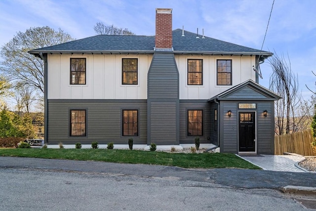 modern farmhouse with a chimney, board and batten siding, roof with shingles, and fence