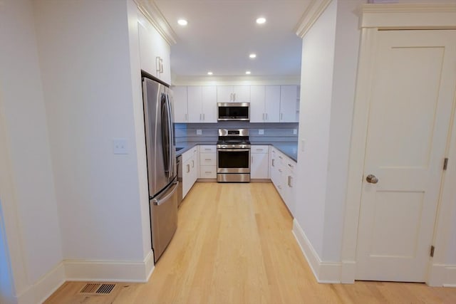 kitchen with decorative backsplash, stainless steel appliances, light wood-style floors, white cabinetry, and dark countertops