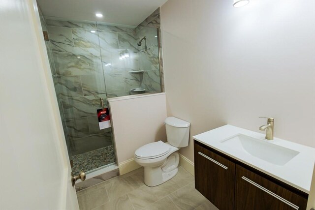 full bathroom featuring toilet, a marble finish shower, vanity, and baseboards