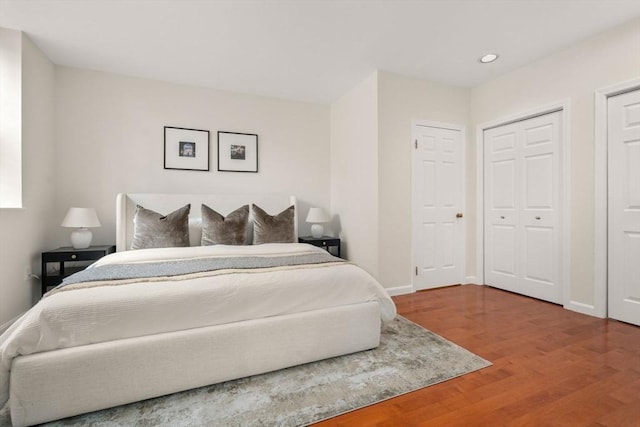 bedroom with wood finished floors, two closets, baseboards, and recessed lighting