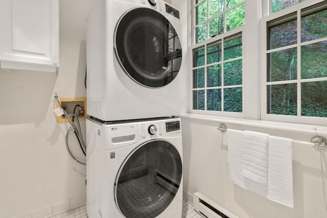 laundry room featuring estacked washer and dryer, cabinet space, tile patterned floors, and baseboards
