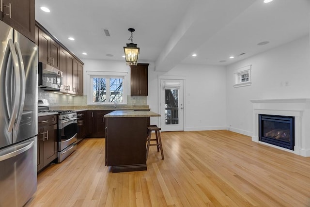 kitchen with a kitchen breakfast bar, light wood-type flooring, a kitchen island, pendant lighting, and stainless steel appliances