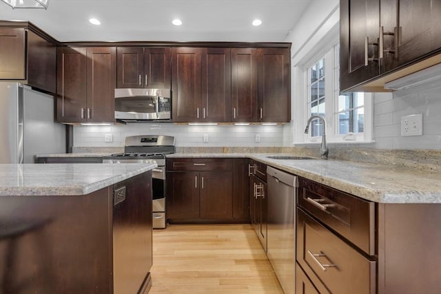 kitchen with stainless steel appliances, tasteful backsplash, sink, and light wood-type flooring