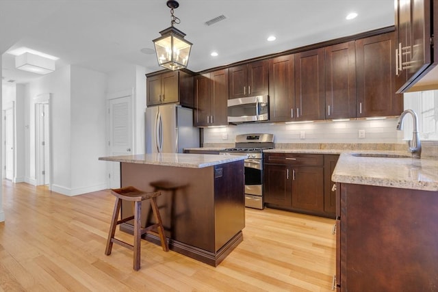 kitchen featuring sink, light hardwood / wood-style flooring, hanging light fixtures, stainless steel appliances, and a center island