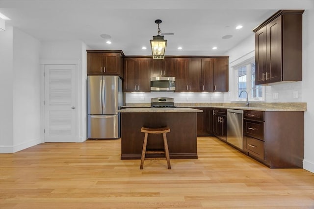 kitchen with stainless steel appliances, decorative light fixtures, a center island, and light wood-type flooring