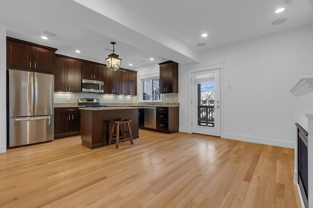 kitchen featuring a breakfast bar area, decorative light fixtures, a center island, light wood-type flooring, and stainless steel appliances