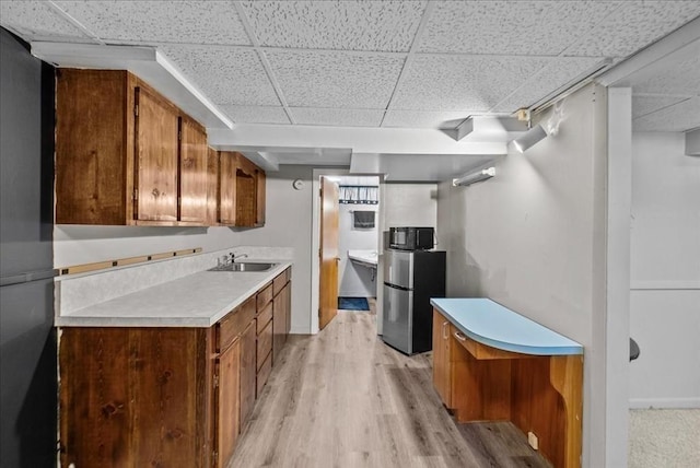 kitchen with a sink, light wood finished floors, light countertops, freestanding refrigerator, and a drop ceiling
