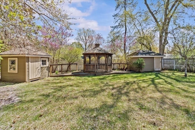 view of yard featuring a deck, a gazebo, an outdoor structure, a fenced backyard, and a shed