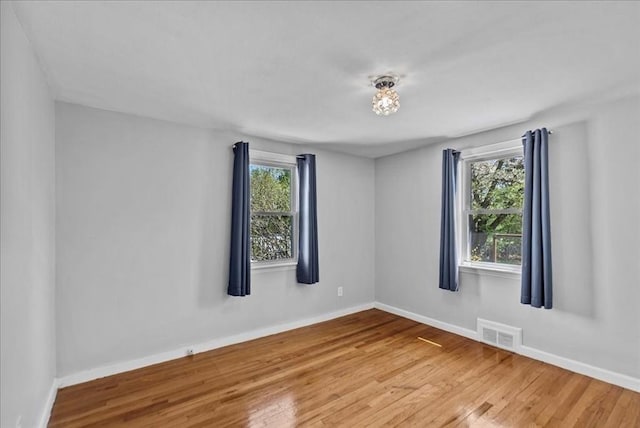 empty room with visible vents, a healthy amount of sunlight, and wood finished floors