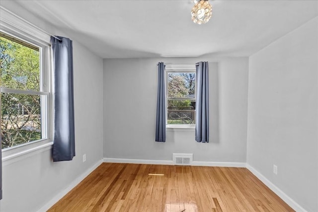 empty room featuring visible vents, baseboards, wood finished floors, and a healthy amount of sunlight