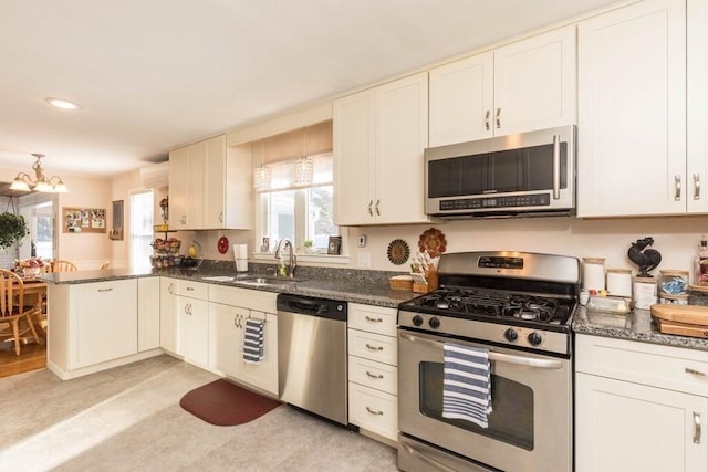 kitchen with stainless steel appliances, sink, dark stone countertops, and kitchen peninsula